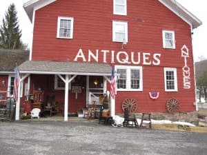 A red building with large white letters spelling "ANTIQUES," featuring a porch and various vintage items displayed outside. A red building with large white letters spelling "ANTIQUES," featuring a porch and various vintage items displayed outside.