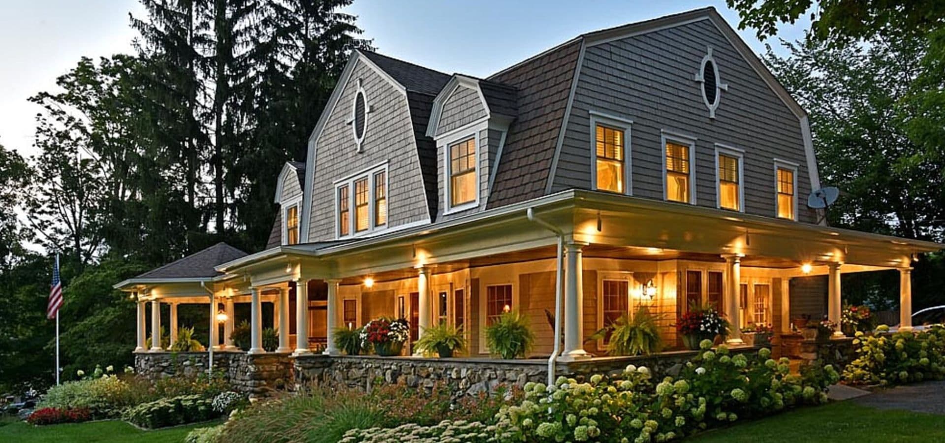 A charming two-story house with a porch and garden, illuminated at dusk.