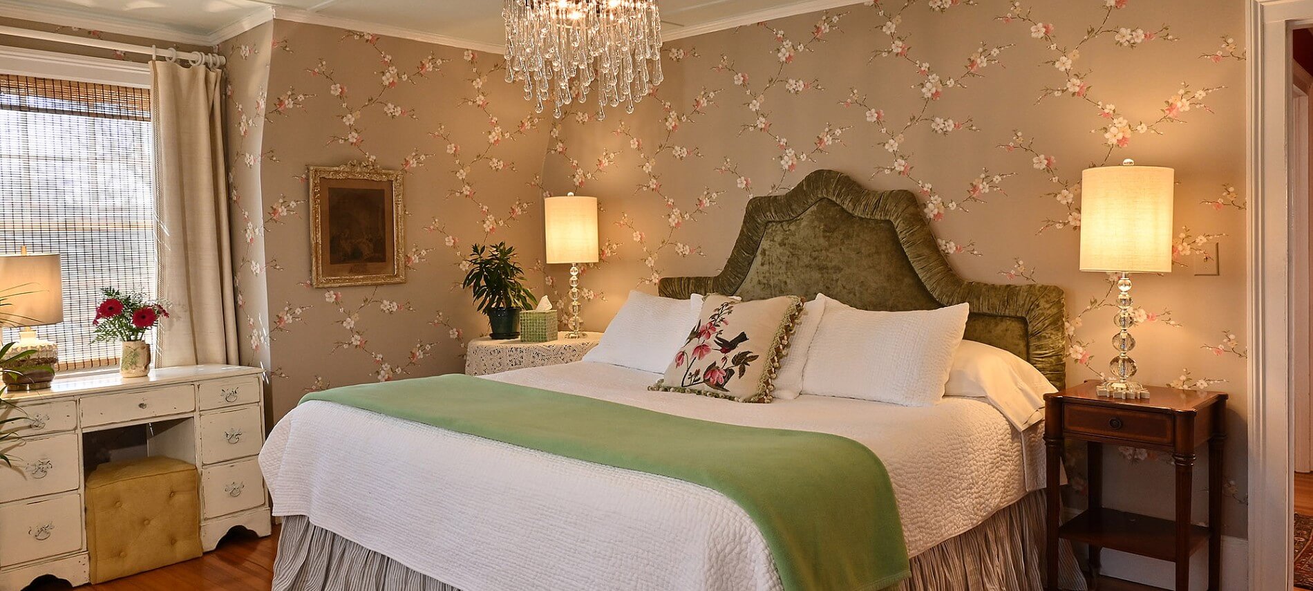 Elegant guest room with queen bed, white duvet cover, flowered wallpaper and chandelier light on ceiling